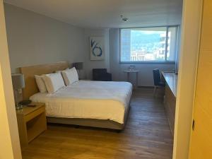 a bedroom with a bed and a desk and a window at Hotel Estelar Blue in Medellín