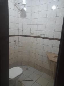 a white tiled bathroom with a toilet and a sink at Quarto para temporada in Ribeirão Preto