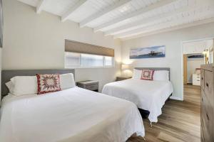 two beds in a bedroom with white walls and wood floors at ON THE SAND!! Private Beach! OCEAN FRONT HOT TUB!! in Dana Point