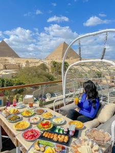 a woman sitting at a table with food in front of pyramids at Tree Lounge Pyramids View INN , Sphinx Giza in Cairo