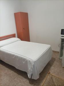 1 dormitorio con cama blanca y armario de madera en PENSIÓN CARLOS III, en Tomelloso