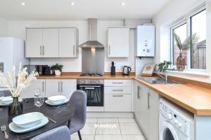a kitchen with white cabinets and a table with chairs at Denton House by Truestays - NEW 3 Bedroom House in Manchester in Manchester