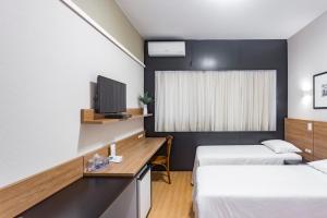 a room with two beds and a desk with a tv at Cambirela Hotel in Florianópolis