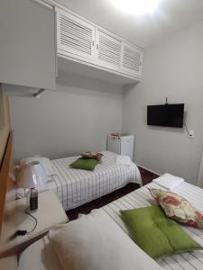 2 bedden in een witte kamer met een tv bij suite in Itanhaém