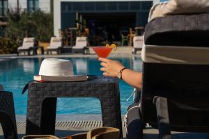 une personne tenant un verre sur une table à côté d'une piscine dans l'établissement Kotinos Beach Hotel, à Çanakkale