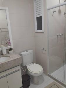 La salle de bains blanche est pourvue d'une douche et de toilettes. dans l'établissement Apartamento Arraial do Cabo, à Arraial do Cabo