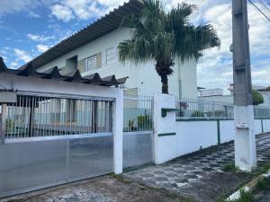 a white house with a fence and a palm tree at Apto/garagem coberta/900m-Centro in Registro