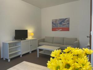 Haus Check-In في غوترسلوه: غرفة معيشة بها أريكة وتلفزيون وورود صفراء