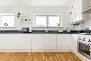 a white kitchen with white cabinets and black counter tops at Modern 2 Bed Apartment London Lewisham - Perfect for Long Stays in London