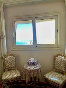 two chairs and a table in a room with two windows at Lovely apartment in Alexandria