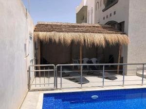 a patio with a straw umbrella and a swimming pool at La villa H in Houmt Souk