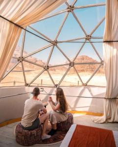 Ein Mann und eine Frau sitzen in einem Zimmer mit Fenster in der Unterkunft Desert relax camp in Wadi Rum