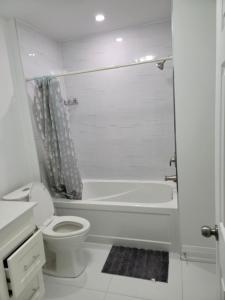 a white bathroom with a toilet and a bath tub at Beautiful Langston Home in Brampton