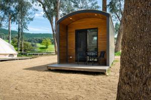 a small wooden cabin with a table and chairs in front of a tree at Bright Cabin Park in Bright