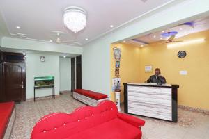 Un uomo in piedi davanti a un bancone in un atrio con un divano rosso di OYO Flagship Hotel Kothiwal a Muthiganj