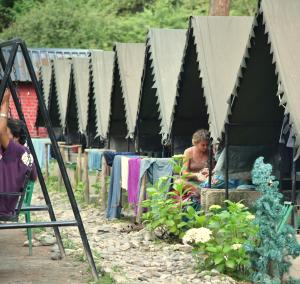 uma mulher sentada numa tenda preta com uma mulher sentada num jardim em Himtrek Riverside Camps, Kasol em Kasol