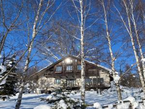 una cabaña de madera en la nieve con árboles en Pension Raclette en Nakafurano