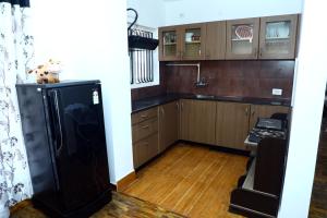 cocina con armarios de madera y nevera negra en HAILSTONE HOME STAY en Ooty