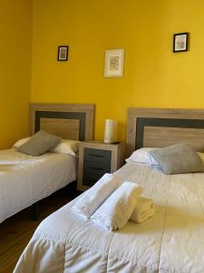 2 camas en una habitación con paredes amarillas en Hotel Restaurante Agapio de TRESNIÑO en Quintanilla de Onésimo