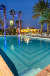 a swimming pool with palm trees and chairs at night at Kenzi Azghor in Ouarzazate