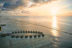 eine Gruppe von Sonnenschirmen am Strand bei Sonnenuntergang in der Unterkunft COMO Maalifushi - Partner Travels FREE for 7 Nights or More in Maalifushi