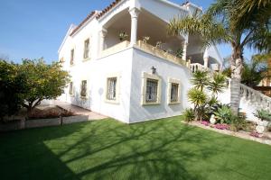 een wit huis met een groene tuin met palmbomen bij Villa Gladiols in Cambrils