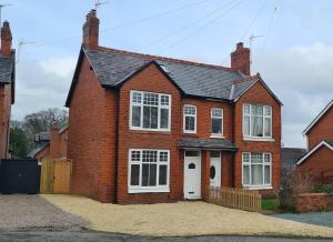uma casa de tijolos vermelhos com uma porta branca em Village Life, cosy yet spacious home em Oswestry