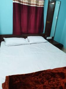 a bedroom with a white bed with a red curtain at Hotel Ambika in Deoghar