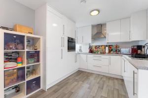 una cucina bianca con armadi bianchi e pavimenti in legno di Tranquility a Cheam