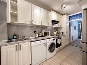 cocina con armarios blancos, lavadora y secadora en Charming 3-bedroom family home en Londres