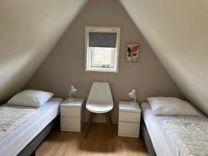 2 Betten in einem Dachzimmer mit einem Stuhl und einem Fenster in der Unterkunft Vakantiehuis Sofie Lauwersmeer met sauna in Anjum