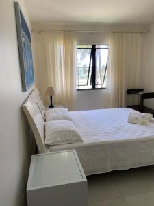 ein weißes Bett in einem Schlafzimmer mit einem Fenster in der Unterkunft Seu cantinho no paraíso de Guarajuba - Bahia in Guarajuba