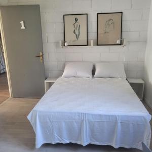 een slaapkamer met een wit bed met twee foto's aan de muur bij Le Jardin De Nicolas in Couret