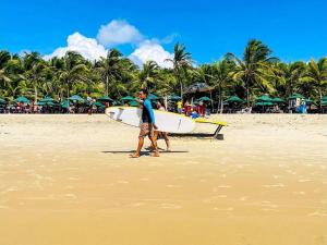 un uomo che cammina sulla spiaggia con una tavola da surf di Hospedaria da Praia Fortaleza a Fortaleza