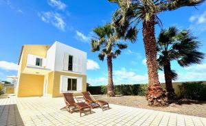 duas cadeiras e palmeiras em frente a uma casa em Profetas GuestHouse em Porto Santo