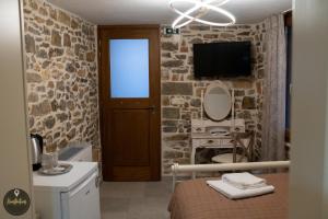 Dormitorio con pared de piedra, cama y TV en SKINOS rooms and apartment en Pyrgi