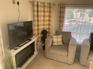 a living room with a flat screen tv and two chairs at Gold star 6 birth caravan in Berrow