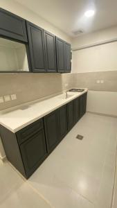 a kitchen with black cabinets and a white tile floor at هوتيل القصيم 2 للشقق الفندقية in Buraydah