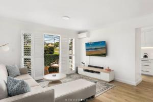 a white living room with a couch and a table at Stylish Beachside Sanctuary, steps to the beach in Sydney