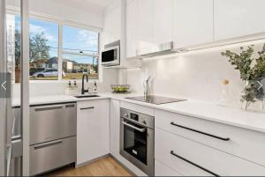 a white kitchen with a sink and a stove at Stylish Beachside Sanctuary, steps to the beach in Sydney