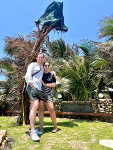 a man and a woman standing in front of a palm tree at Sầm Sơn Boutique Hotel Phan Thiết in Phan Thiet