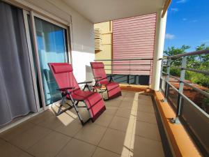 2 sillas rojas sentadas en un balcón con vistas en T3 Cocooning au Neptune Saint Gilles-Les-Bains en Saint-Gilles-les-Bains