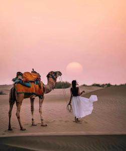 a woman standing next to a camel in the desert at Jaisalmer Sam Sand Dunes Luxury Camps in Jaisalmer