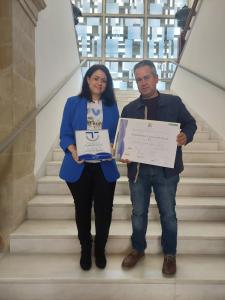 un hombre y una mujer de pie en las escaleras con certificados en Apartamentos Turísticos El AOVE en Baeza