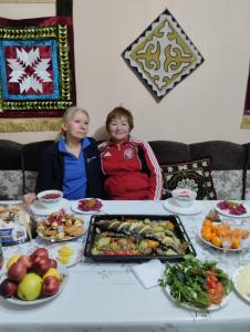 zwei Frauen sitzen an einem Tisch mit Essen drauf in der Unterkunft Guest House Dinara in Kaji-Say