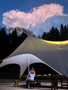 a woman sitting on a bench under a large tent at Zhangjiajie National Forest Park Camping in Zhangjiajie
