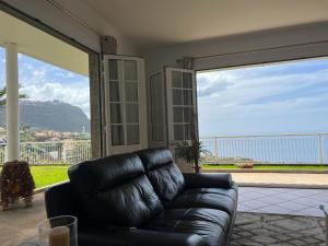 ein schwarzes Ledersofa in einem Wohnzimmer mit einem großen Fenster in der Unterkunft Spring House AL in Arco da Calheta