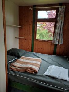 Ce lit se trouve dans un dortoir doté d'une fenêtre et d'une couverture. dans l'établissement Camping la Vallée, à La Tour-dʼAuvergne