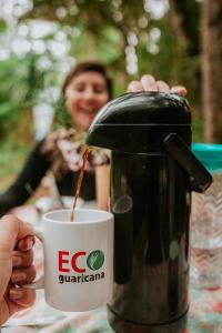 una persona sosteniendo una cafetera junto a una taza en Bosque Contêiner Eco Guaricana en São José dos Pinhais