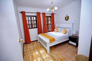 um quarto com uma cama branca e cortinas cor de laranja em Peaceful and Cozy Home in Arusha em Ngateu